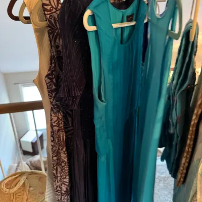 Sale Photo Thumbnail #158: Selection of women's dresses, including a bright turquoise sleeveless dress and a patterned brown and white dress, hanging on a clothing rack.