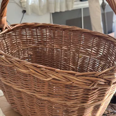 Sale Photo Thumbnail #209: Large oval woven wicker basket with a sturdy arched carrying handle, showing a natural warm brown finish.