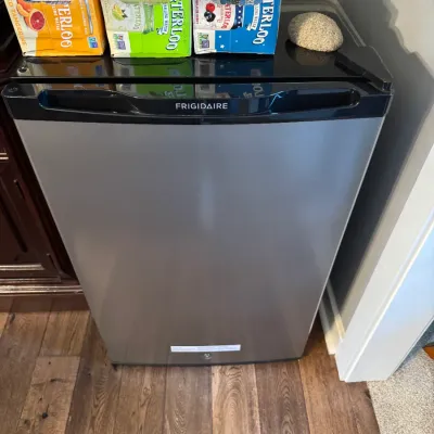 Sale Photo Thumbnail #239: Frigidaire compact mini-fridge with a stainless steel door and black trim, shown with cases of Waterloo sparkling water on top.