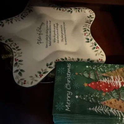 Sale Photo Thumbnail #256: Christmas-themed ceramic "Plate of Sharing" shaped like a star with holly leaf borders, paired with a stack of green "Merry Christmas" paper napkins.