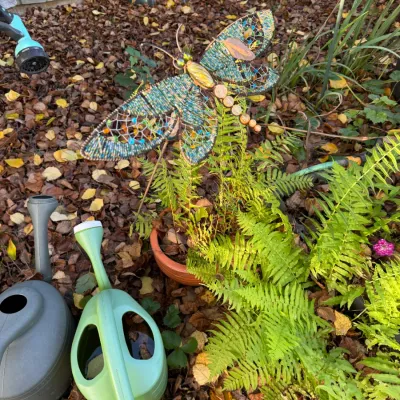 Sale Photo Thumbnail #275: Decorative beaded wire dragonfly garden stake, shown alongside potted ferns and plastic watering cans.