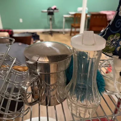 Sale Photo Thumbnail #101: Vintage stainless steel sugar dispenser with a hinged lid alongside a clear glass syrup dispenser featuring a white plastic pour-spout lid.
