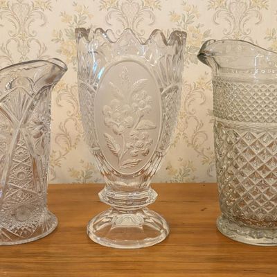 Sale Photo Thumbnail #639: A Trio of Colorless Decorative Pressed Glassware Including Two Pitchers and a Footed Vase