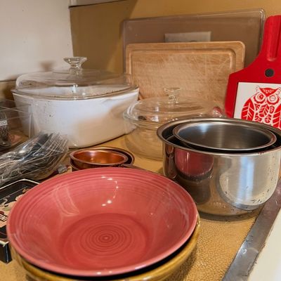 Collection of kitchenware featuring a pink Fiesta ceramic bowl, vintage Corning Ware roaster with glass lid, stainless steel saucepans,...