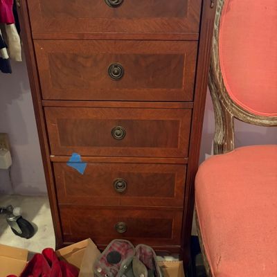 Traditional five-drawer wood lingerie chest featuring decorative inlay and brass ring pulls, shown alongside an upholstered armchair.