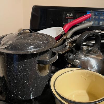 Assorted cookware collection including a black speckle enamel stockpot, stainless steel teakettle, enamel mixing bowls, and frying pans.