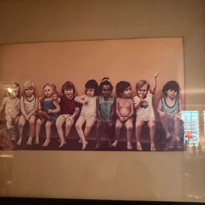 Framed vintage art print depicting a row of young children sitting together on a bench, housed under glass in a dark wooden frame.