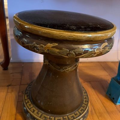 Vintage ceramic garden seat or pedestal with a dark glaze, leaf relief accents, and a Greek key border near the base.