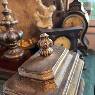Vintage gilt wood box with an ornate carved finial lid, displayed alongside antique clocks and decorative silver accents.