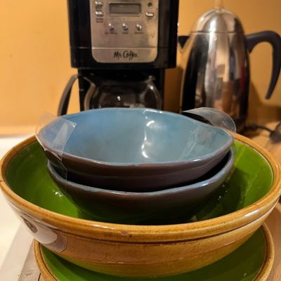 Stack of ceramic kitchenware including blue and brown smaller bowls inside a large yellow-and-green serving bowl, displayed in front of a...