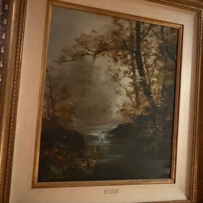 Framed landscape oil painting depicting a misty forest scene with a stream, housed in an ornate gilded wood frame with a linen mat.