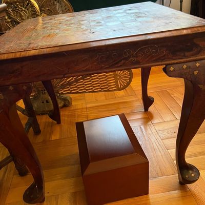 Vintage inlaid wooden game table featuring cabriole legs and brass scroll accents, shown with a small wooden footstool underneath.