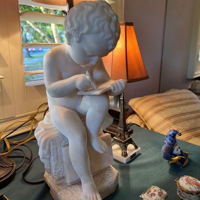 White carved marble or alabaster figure of a seated cherub writing, paired with a small Eiffel Tower novelty lamp and decorative trinket...