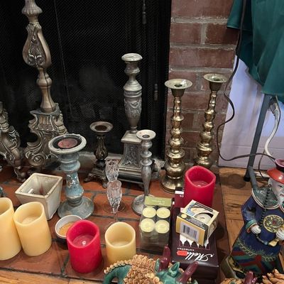 Collection of decorative home accents displayed on a hearth, including metal candlesticks, pillar candles, tea lights, and Asian-style...