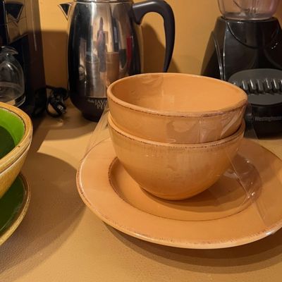 Set of warm yellow ceramic dishware, wrapped in plastic, sitting on a countertop alongside small kitchen appliances.