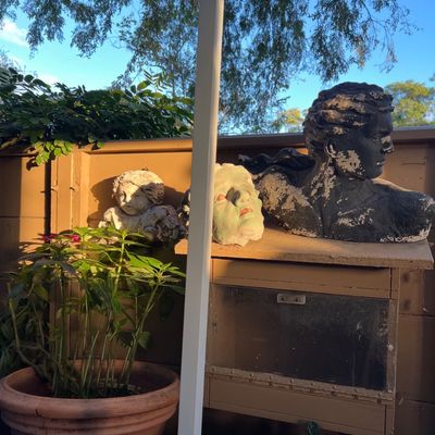 Collection of outdoor garden sculptures and busts, including a cherub figure, a painted face sculpture, and a distressed classical-style...