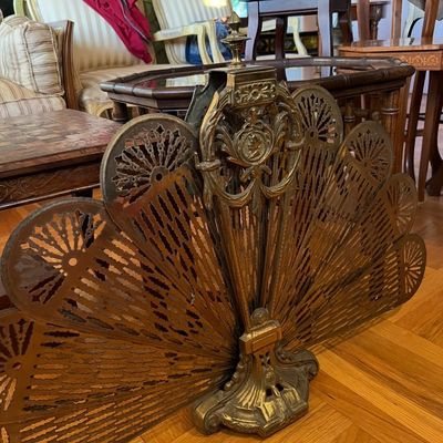 Vintage ornate brass peacock folding fireplace screen, featuring intricate filigree fan panels and an ornate central crest.