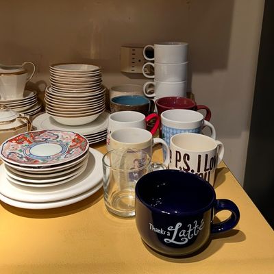 Collection of kitchen dishware, including stacks of bowls, plates, and an assortment of ceramic coffee mugs.