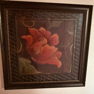 Framed floral print featuring a stylized red blossom set against a dark background, enclosed in an ornate dark wood frame.