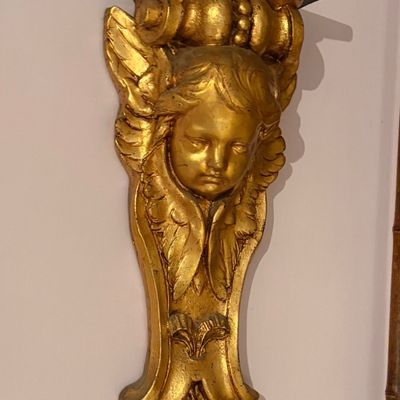 Giltwood cherub wall bracket shelf in Baroque style, featuring a detailed winged seraph face and a black top shelf surface.