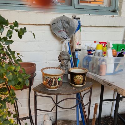 Collection of outdoor items including decorative Asian-style planters, a Beethoven bust, a metal plant stand, and various cleaning supplies.