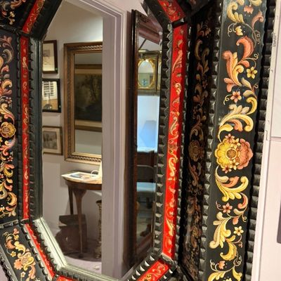 Hand-painted octagonal wall mirror featuring intricate floral scrollwork motifs in red, gold, and black tones.