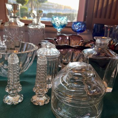 Collection of vintage cut glass and crystal glassware, including decanters, salt shakers, covered jars, and colorful accent pieces...