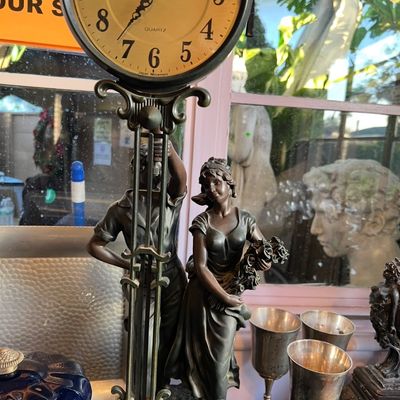 Vintage-style decorative bronze-tone quartz clock featuring figures of a man and a woman holding flowers.
