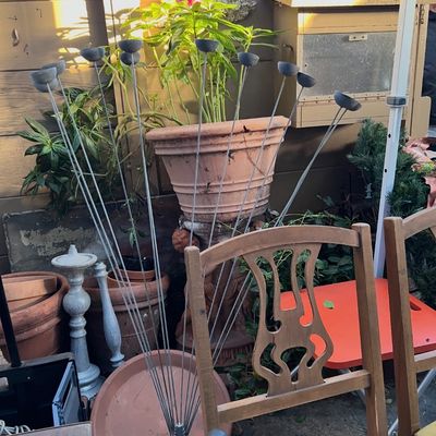 A metal multi-stem candle or oil lamp stand with cupped holders, set among terracotta planters and wooden dining chairs.