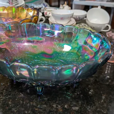 Sale Photo Thumbnail #4: Vintage footed carnival glass bowl with a scalloped edge and vibrant iridescent blue, green, and pink tones, shown alongside other glassware and teacups.