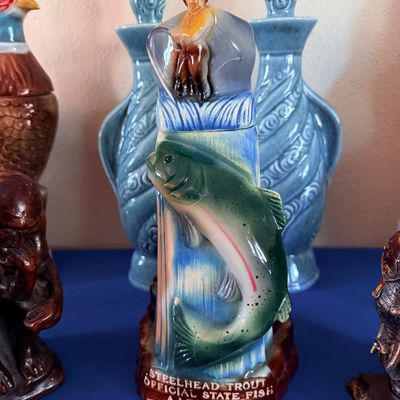 Sale Photo Thumbnail #13: Vintage ceramic decanter featuring a Steelhead Trout and fisherman, celebrating Washington State, flanked by other collectible decanters.