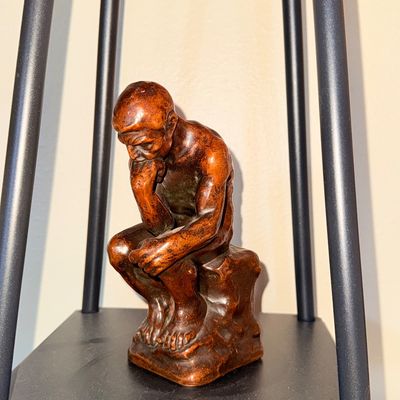 Sale Photo Thumbnail #22: Small replica sculpture of Auguste Rodin's "The Thinker" with a bronze-look finish, displayed on a black metal shelf.