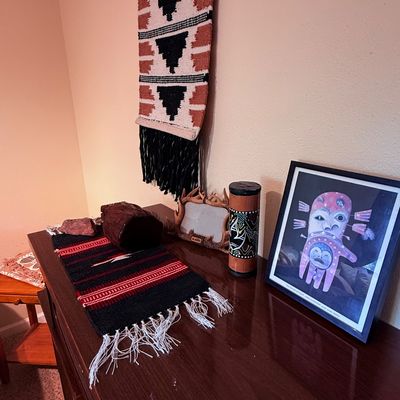 Sale Photo Thumbnail #10: Collection of Southwestern and Indigenous-style decor, including a woven wall hanging, a small patterned table runner, a framed print of an Alaska Native mask, and a decorative rainstick.