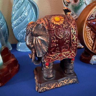 Sale Photo Thumbnail #12: Ornate elephant figurine with a decorative red and gold blanket, displayed alongside various ceramic vases and collectibles.