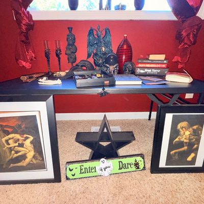 Sale Photo Thumbnail #24: Collection of gothic and occult-themed decor, including framed prints of classical artwork, a Baphomet statue, skull motifs, horror books, and a pentagram shelf.
