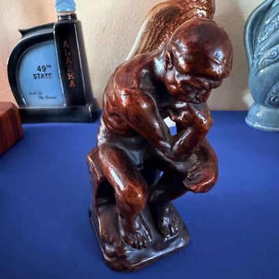Sale Photo Thumbnail #17: Vintage ceramic replica of Rodin's "The Thinker" statue with a glossy brown glaze, displayed alongside collectible decanters.