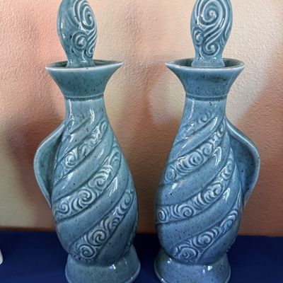 Sale Photo Thumbnail #14: Pair of mid-century ceramic decanters in a speckled light blue glaze, featuring a spiral scroll pattern and matching flame-style stoppers.