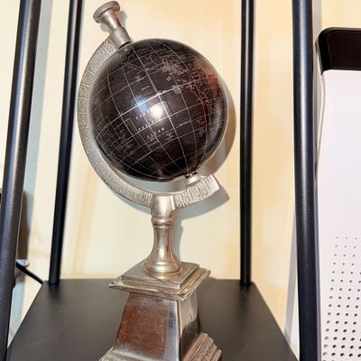 Sale Photo Thumbnail #21: Decorative desk globe featuring a black sphere with silver-toned map lines, mounted on a silver-finished metal stand and base.