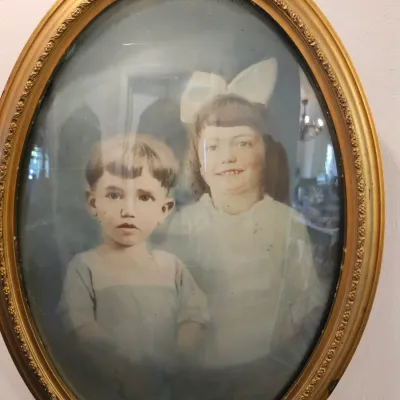 Antique hand-colored portrait of two children, housed in an ornate oval gilt frame with convex bubble glass, circa early 20th century.