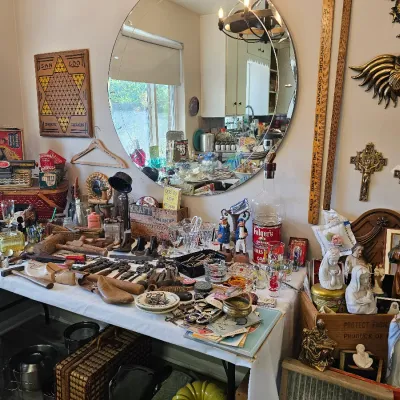 Assortment of vintage collectibles, including religious figurines, wooden shoe lasts, glassware, and wall decor displayed on tables.