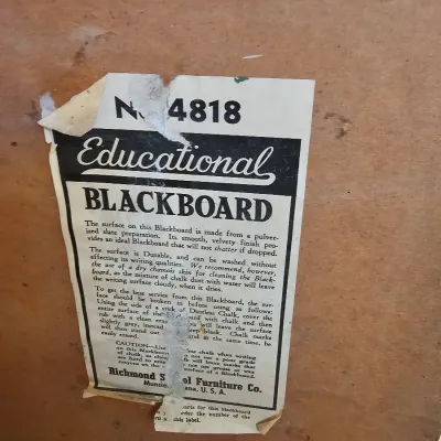 Vintage Richmond School Furniture Co. educational blackboard label, model No. 4818, showing wear and tear on the back of a wooden board.
