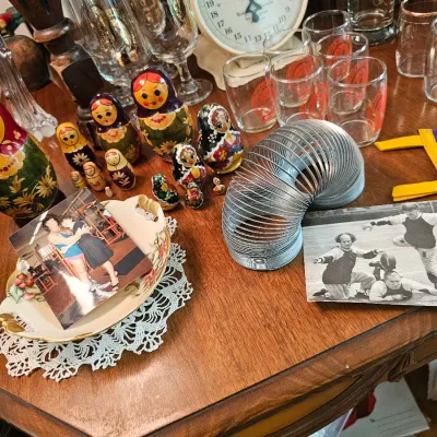 Assorted vintage collectibles including Russian nesting dolls, a metal Slinky toy, old photographs, glassware, and a small felt pennant...