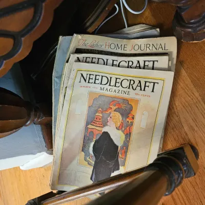 Stack of vintage magazines, including an October 1928 issue of Needlecraft Magazine and a copy of The Ladies' Home Journal, showing...