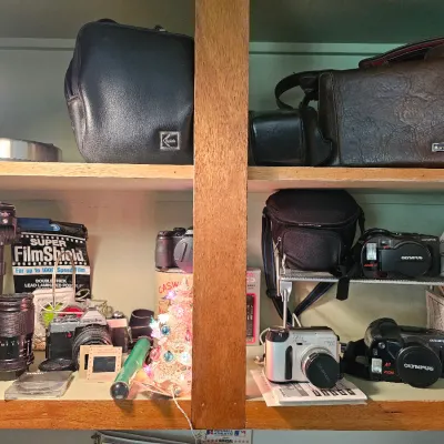 Assorted vintage camera equipment, including Minolta and Olympus SLR and point-and-shoot cameras, lenses, carrying cases, and accessories...
