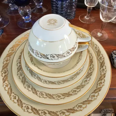 Noritake fine china place setting featuring a cream base with elegant gold leaf and vine borders, topped with a matching teacup.