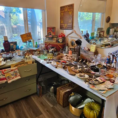 Assortment of vintage collectibles and kitchenware displayed on tables, including glassware, wooden shoe lasts, a vintage typewriter, and...