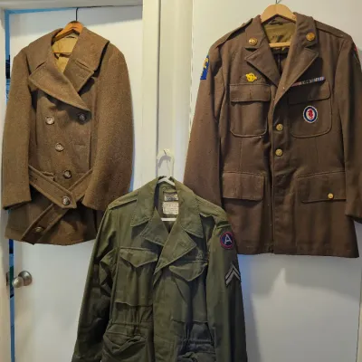 Three vintage military jackets, including a brown wool double-breasted overcoat, a brown dress uniform jacket with patches and ribbons,...