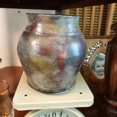 Hand-thrown studio pottery vase with a metallic raku-style glaze, displayed on an antique American Family scale.