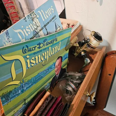 Vintage Walt Disney's Guide to Disneyland booklet and Disney News magazine, displayed alongside a gold-toned spinning fishing reel...