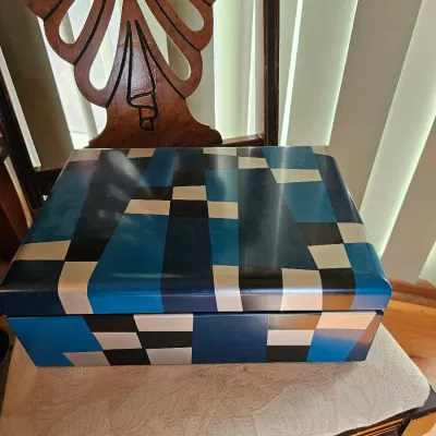Vintage decorative wooden box featuring a hand-painted geometric pattern in shades of blue, black, and silver, resting on a carved wooden...